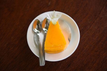 cake slice on white palte with flower and spoon on wooden table background / delicious orange cakeの写真素材