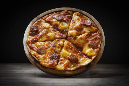 pizza on wooden plate delicious tasty fast food italian traditional pizza cheese with Mozzarella , Smoked pork sausage , Pineapple ham on topping sauce Restaurants or pizzerias on the dark backgroundの写真素材