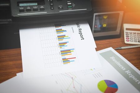 printer printing business reports sale and pile of documents report graph chart on a table at office