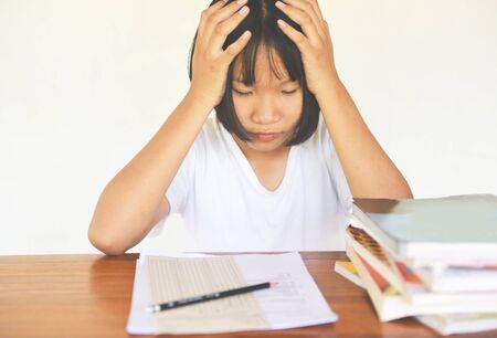 exam stress / education young female college in class taking notes and using a pencil sitting learning concept stressed student girl asian take the exam final with books on the tableの写真素材