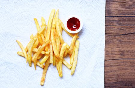 French fries on white paper with ketchup on wooden background