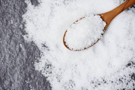 Salt in wooden spoon and heap of white salt on dark background top view , selective focusの写真素材