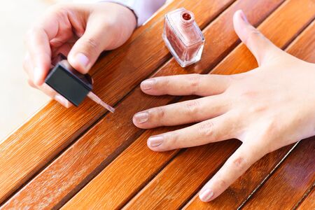 Female hands doing nail polish / woman hand and nail varnish on wooden backgroundの写真素材