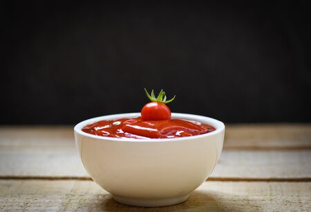 Fresh tomatoes on ketchup in cup tomato sauce on wooden and black background , selective focus