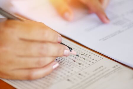 take the exam final high school hand student holding pencil writing on paper answer sheet /...