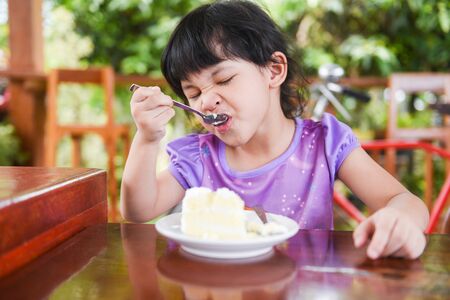 Cute little girl eating cake / Asian child happy and holding a spoon into the mouth with cake on dining table , selective focusの写真素材