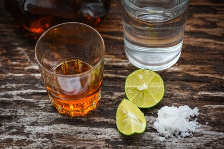 alcoholic drinks and lemon salt on rustic wood background / brandy in a glass with alcohol bottles and water - vodka rum cognac tequila and whiskey conceptの写真素材