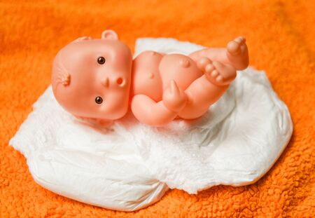 Newborn baby doll with Diapers / baby toy wear white diaper and playing on a orange knitted blanket in the nursery conceptの写真素材