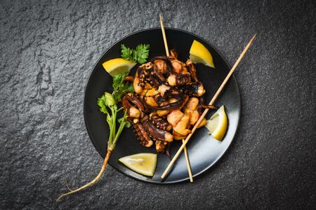 octopus salad with lemon herbs and spices on dark background Tentacles squid grilled appetizer food hot and spicy chilli sauce seafood cooked in skewer sticks served on black plate in the restaurantの写真素材