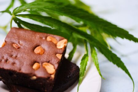 cannabis food snack for health / brownies with marijuana leaf herb on white plate wooden table backgroundの写真素材