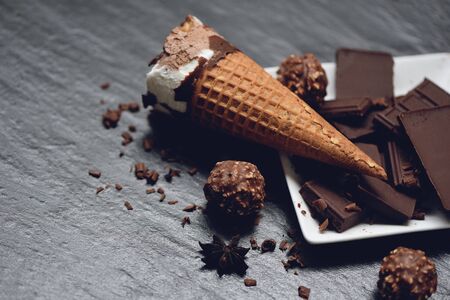 ice cream cone with chocolate bar and ball on dark background / ice cream vanilla covered chocolate frozen sweet dessert or snackの写真素材