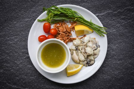 Fresh oysters served on plate and dark background / Oyster Salad with vegetable tomato lemon and herb  seafood sauce in the restaurantの写真素材