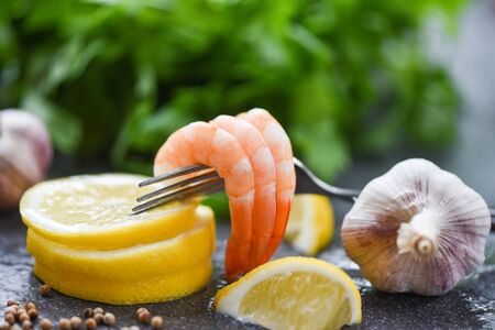 fresh shrimps on fork served on plate / seafood boiled peeled shrimp prawns cooked with spices lemon garlic and vegetable salad lettuce on dark backgroundの写真素材