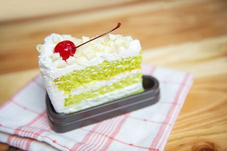 Green cake slice with cherry fruit and cream on white palte on the table / Delicious green tea cheese cakeの写真素材