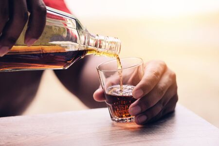 Pouring whiskey or alcohol drink from bottle to glasses on wooden  background / Pour liquorの写真素材