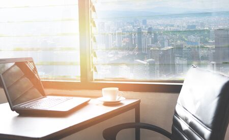 coffee cup on the table in a office with laptop on table in office / Wooden table in sunny office with windows sunlightの写真素材