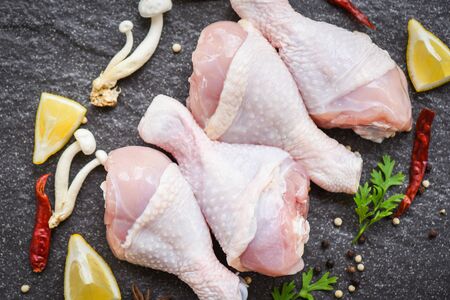 raw chicken legs with lemon chilli herbs and spices and mushroom on black plate  top view / Raw uncooked chicken meat marinated with ingredients for cookingの写真素材