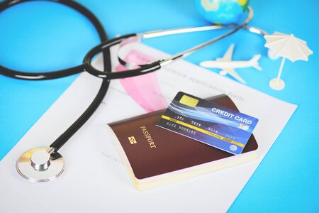 Travel insurance application form with  passport credit cards and stethoscope on blue background / Air travelling for health or global healthcare conceptの写真素材