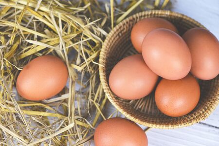 Fresh egg on basket and straw with wooden table background top view / Raw chicken eggs collect from...