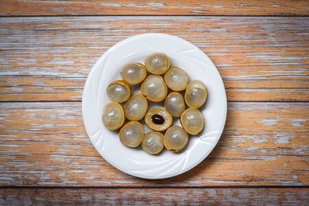 Longan fresh tropical fruit in Thailand / Dimocarpus longan peel exotic fruits on white plate on wooden background , top viewの写真素材