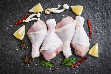 raw chicken legs with lemon chilli herbs and spices and mushroom on black plate  top view / Raw uncooked chicken meat marinated with ingredients for cookingの写真素材