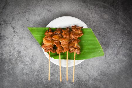Grilled pork thai asian street food style / Slice pork skewer sticks grilled on banana leaf on white plate の写真素材