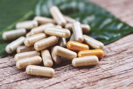 Herbal Medicines / Natural herb capsules on green leaf and rustic background , selective focusの写真素材