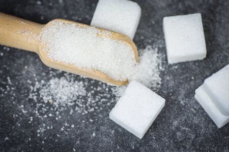 White sugar and sugar cubes on the wooden scoop with dark background, top view selective focusの写真素材