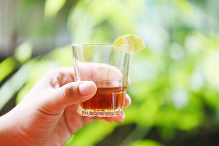 Hand man holding glasses of whiskey or alcohol drink with lemon lime and nature green background
