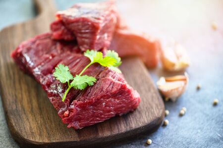 Raw meat beef steak with spices garlic on wooden cutting board and black background, top view /...