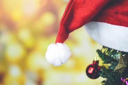 Beautiful decoration christmas hat on blurred background / Christmas tree with santa claus red hat ball gift box star and lights decorated pine tree New Year holidays festival celebrationの写真素材