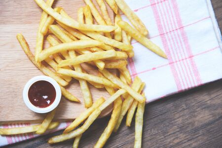 French fries with ketchup on wooden board on dining table