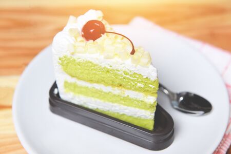 Delicious green tea cheese cake / Green cake slice with cherry fruit and cream on white palte on the...