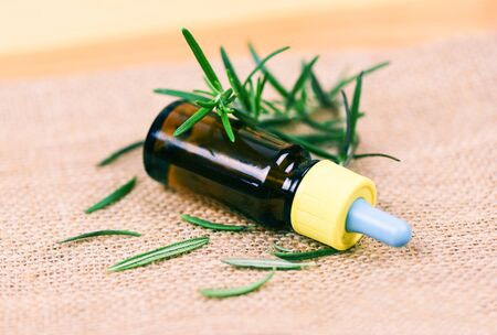 Essential oil bottle natural spa ingredients rosemary oil for aromatherapy and rosemary leaf on sack background / Organic cosmetics with extracts of herbsの写真素材