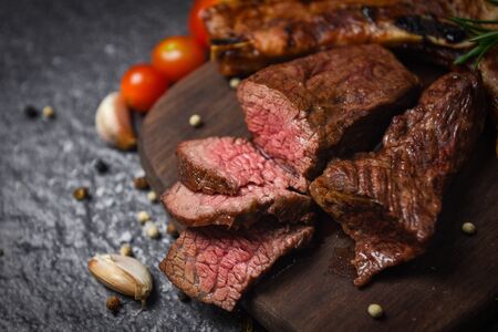 Roasted beef steak fillet with herb and spices served with vegetable on wooden board / grilled beef meat slice on black background の写真素材