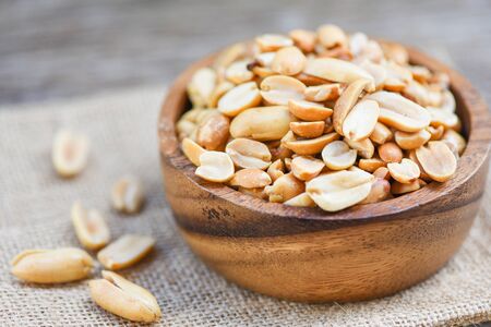 Roasted peanuts on a wooden bowl and sack background / salted peanuts as a food or snack