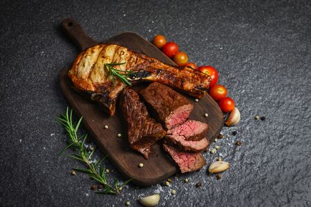 Roasted beef steak fillet and pork chops with herb and spices serve with vegetable on wooden cutting board / grilled beef meat slice on black backgroundの写真素材