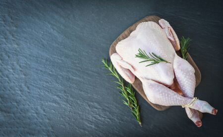 rosemary chicken meat wooden cutting board / fresh raw chicken whole on black plate background , top viewの写真素材