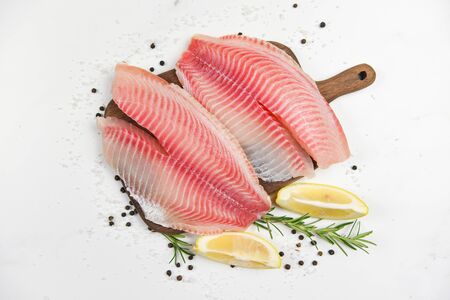 Fresh fish fillet sliced for steak or salad with herbs spices rosemary and lemon / Raw tilapia fillet fish and salt on white stone  background and ingredients for cooking food の写真素材