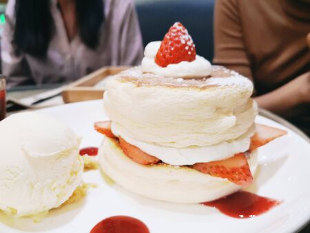 Homemade fluffy pancake and sweet syrup / Delicious pancakes with strawberry sauce and ice cream on dining table in the cafe restaurantの写真素材