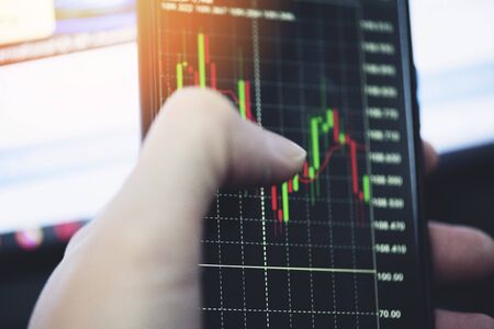 Trading stock graph or forex online with application on smartphone / Businessman trading stocks chart with statistic analysis price table market financial on mobile phone finance data and technologyの写真素材