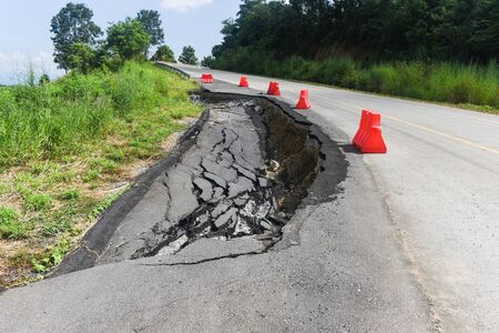 Asphalt road collapsed and cracks in the roadside / Road landslide subside with plastic barriers on uphillの写真素材