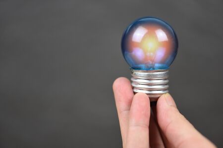 Hand holding light bulb with light from the lamp on black background / energy saving idea , power...