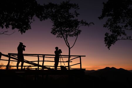 photographer silhouette on the mountain taking photo shooting landscape with sunset or sunrise / photographer woman with cameraの写真素材