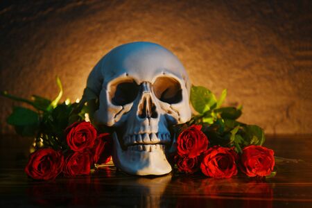 Red roses flower bouquet on rustic wood with skull and candlelight background / flowers rose romantic love and death valentine day conceptの写真素材