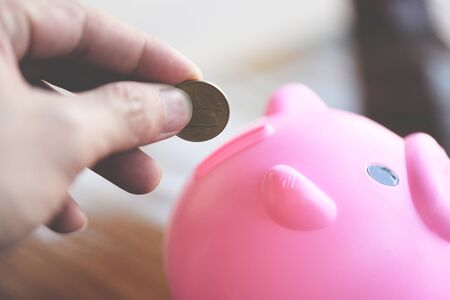 hand man putting money coin into piggy bank at table at home close up / save money for scholarships...