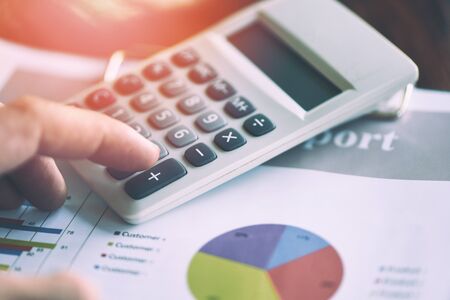 Business man using calculator for report financial statistics documents on infographics at office table close up / Sales report conceptの写真素材