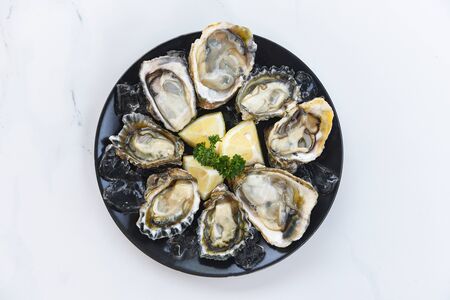 Fresh oysters seafood on a black plate background / Open oyster shell with herb spices lemon...