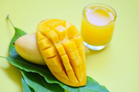 Mango summer juice in glass with sweet ripe slice of mango on green leaves from tree tropical fruit conceptの写真素材