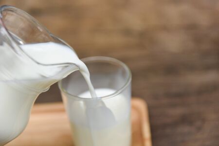 Fresh milk natural in a glass jug and  Pouring milk into glass on wooden background の写真素材